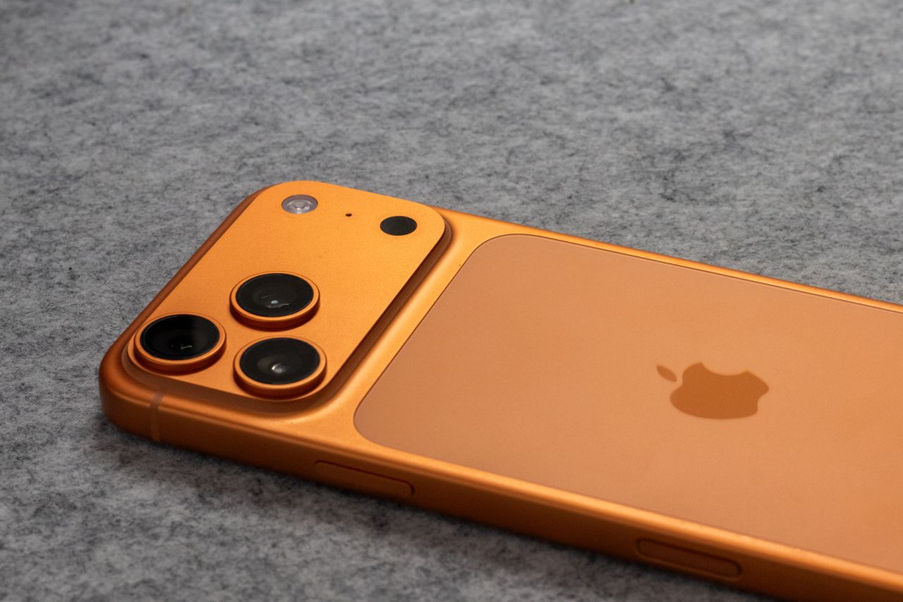 Orange smartphone with dual cameras placed on a soft gray fabric surface.